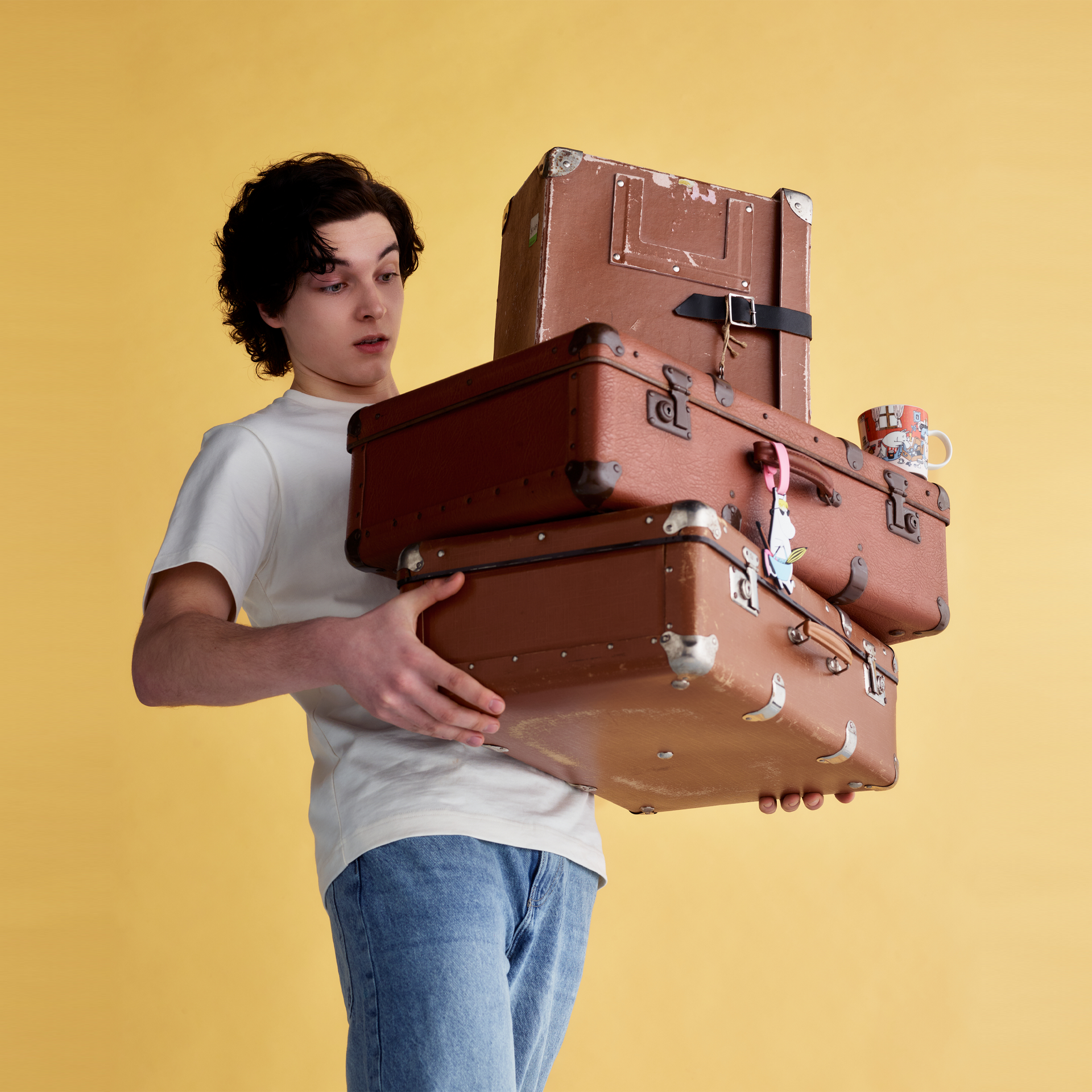 Mummi bagasjelapp Snorkfrøken - Person holding a stack of vintage suitcases against a yellow background