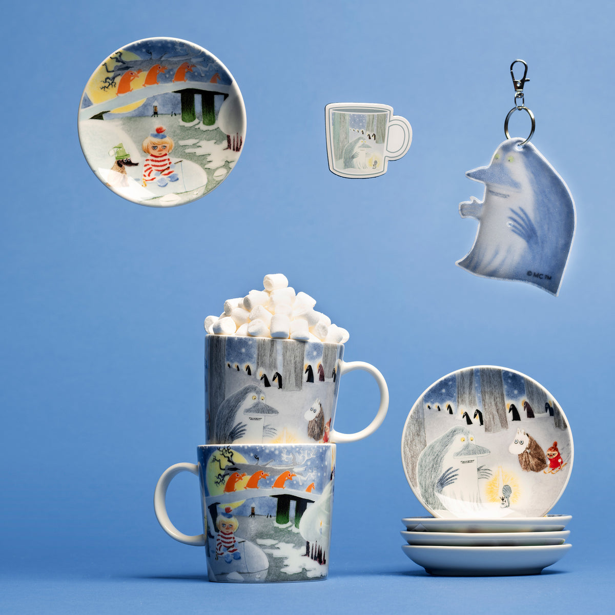 Winternight Glow ceramic mugs, mini plates, reflector and magnet, arranged on a blue studio background. 