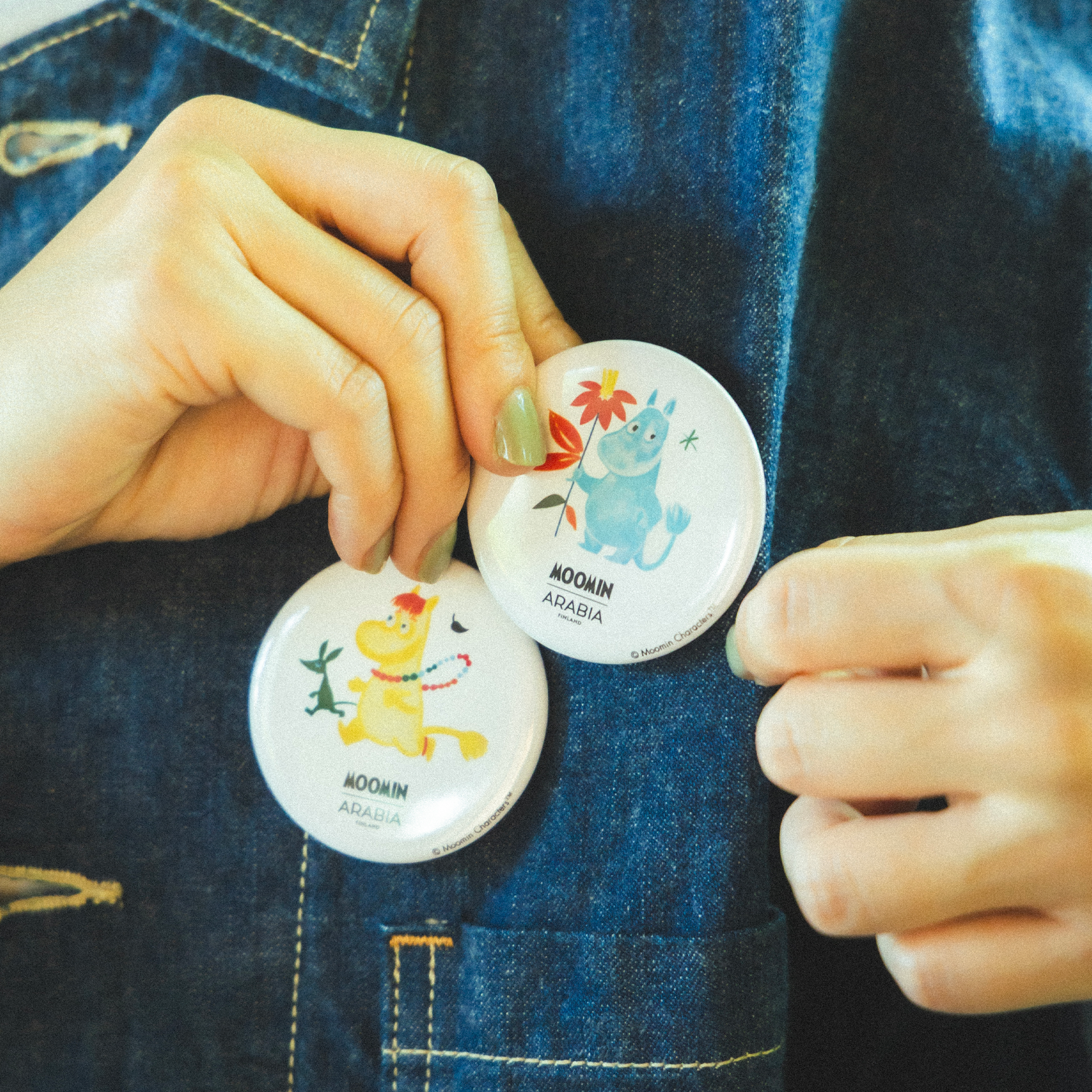 Mummi pinssett Beams -  A person wearing a denim jacket putting on a Snorkmaiden and Moomintroll badges.