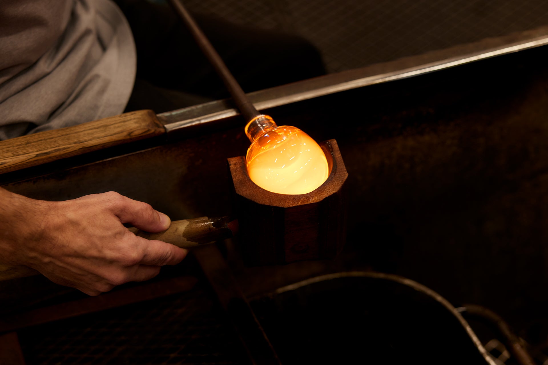Glassblowing process with a molten glass object and tools in an Iittala factory setting.