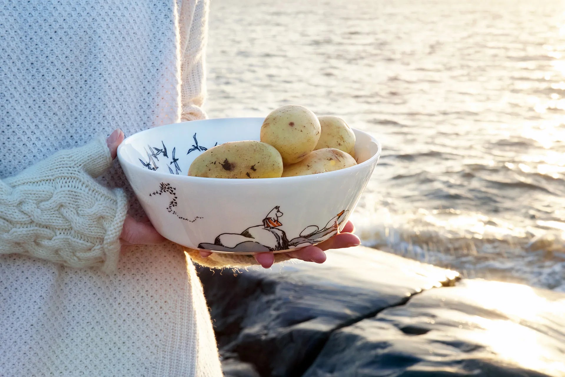 Person holding a bowl of potatoes by a body of water