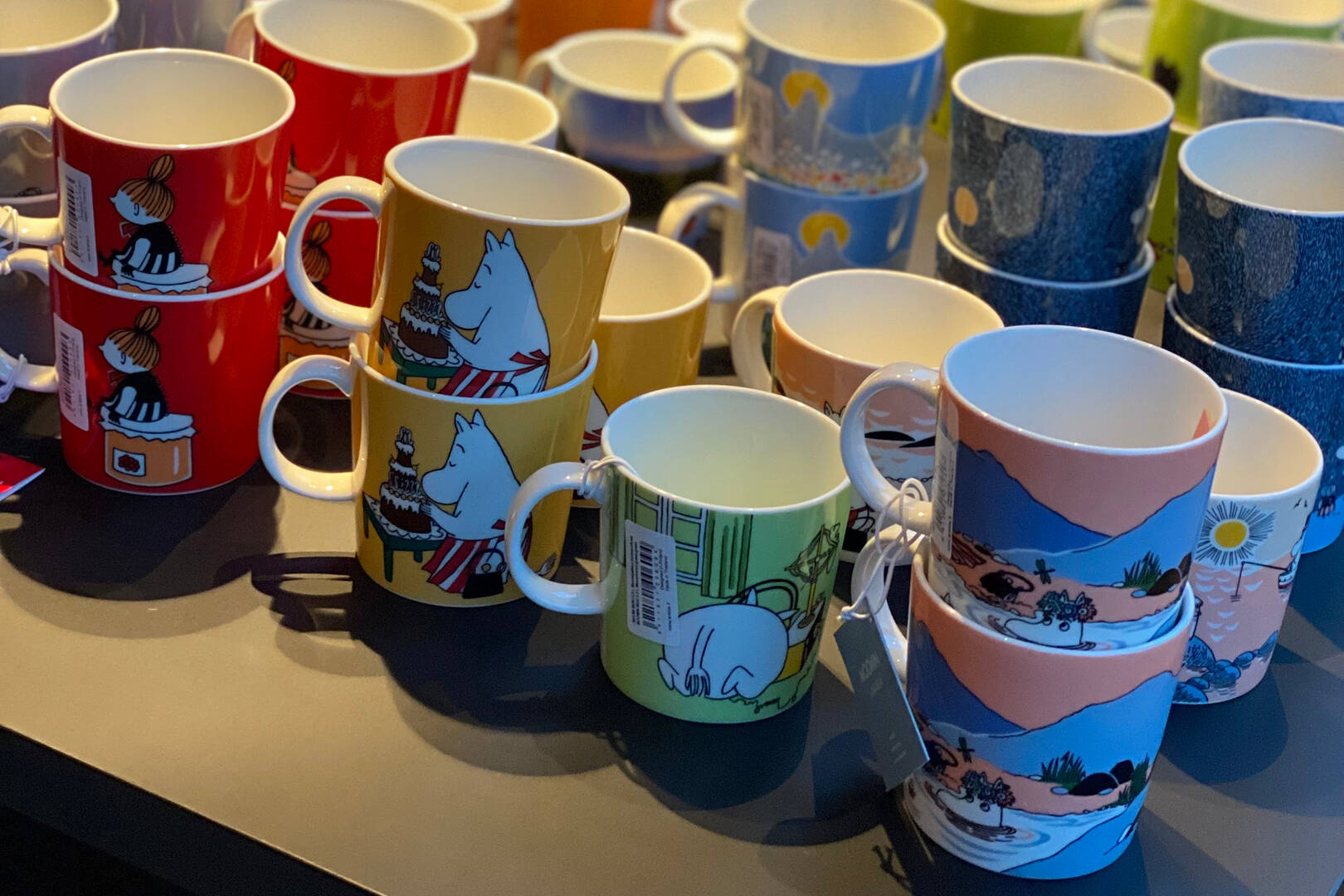 Collection of colorful Moomin mugs with various designs on a reflective surface