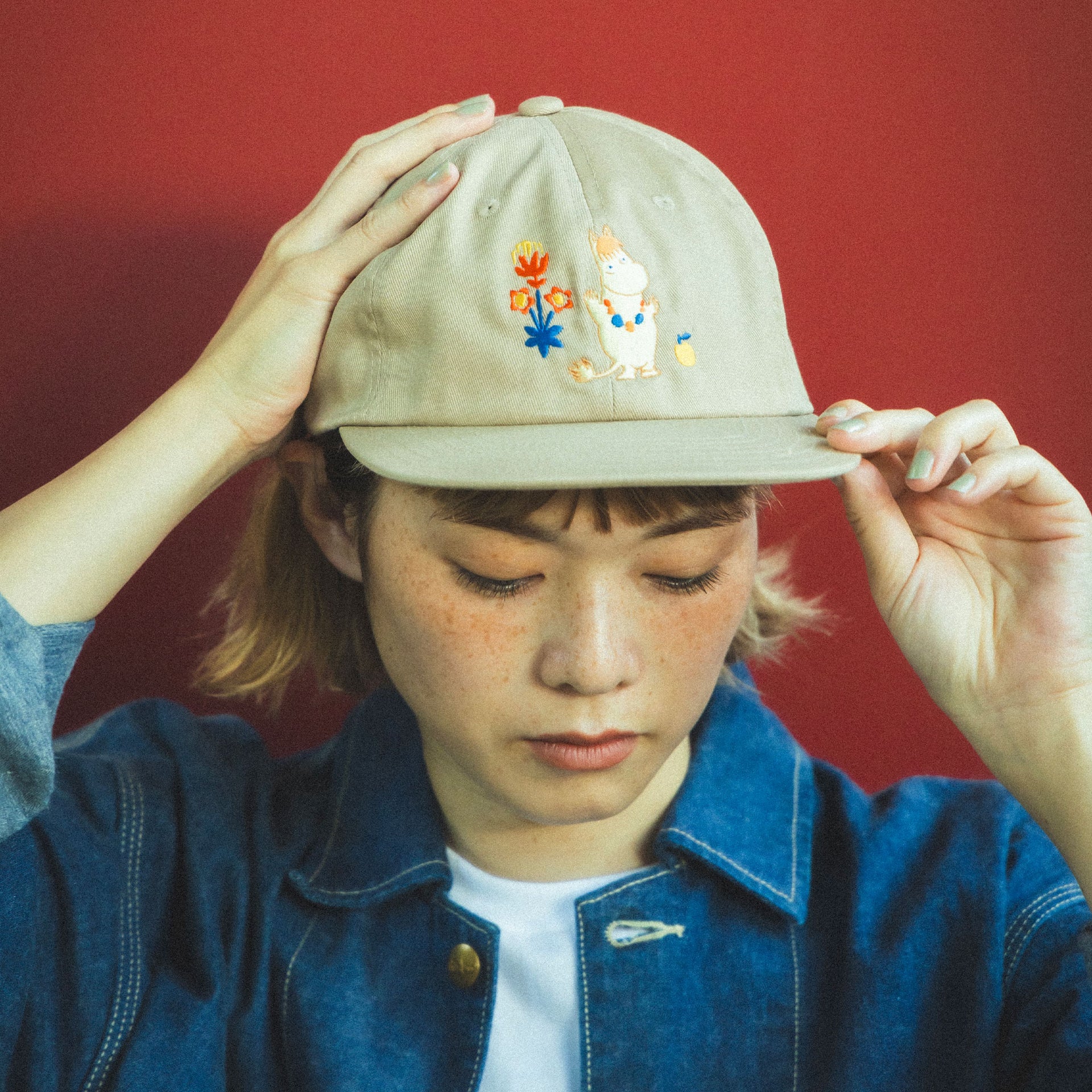 Mummi lue beige Beams - Person wearing a beige cap with Snorkmaiden design against a red background