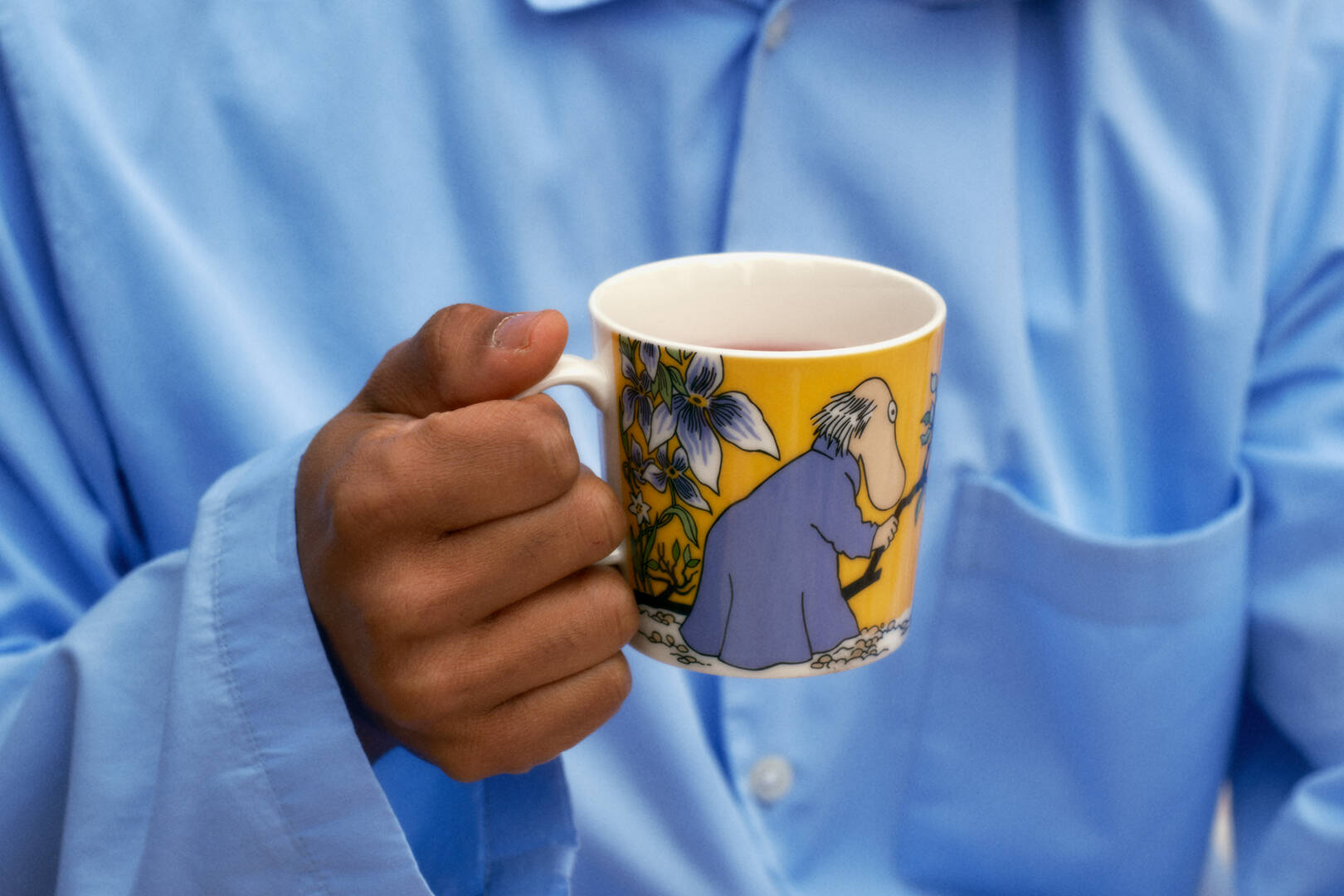 Person holding a yellow Hemulen mug with a colorful design, wearing a blue shirt.