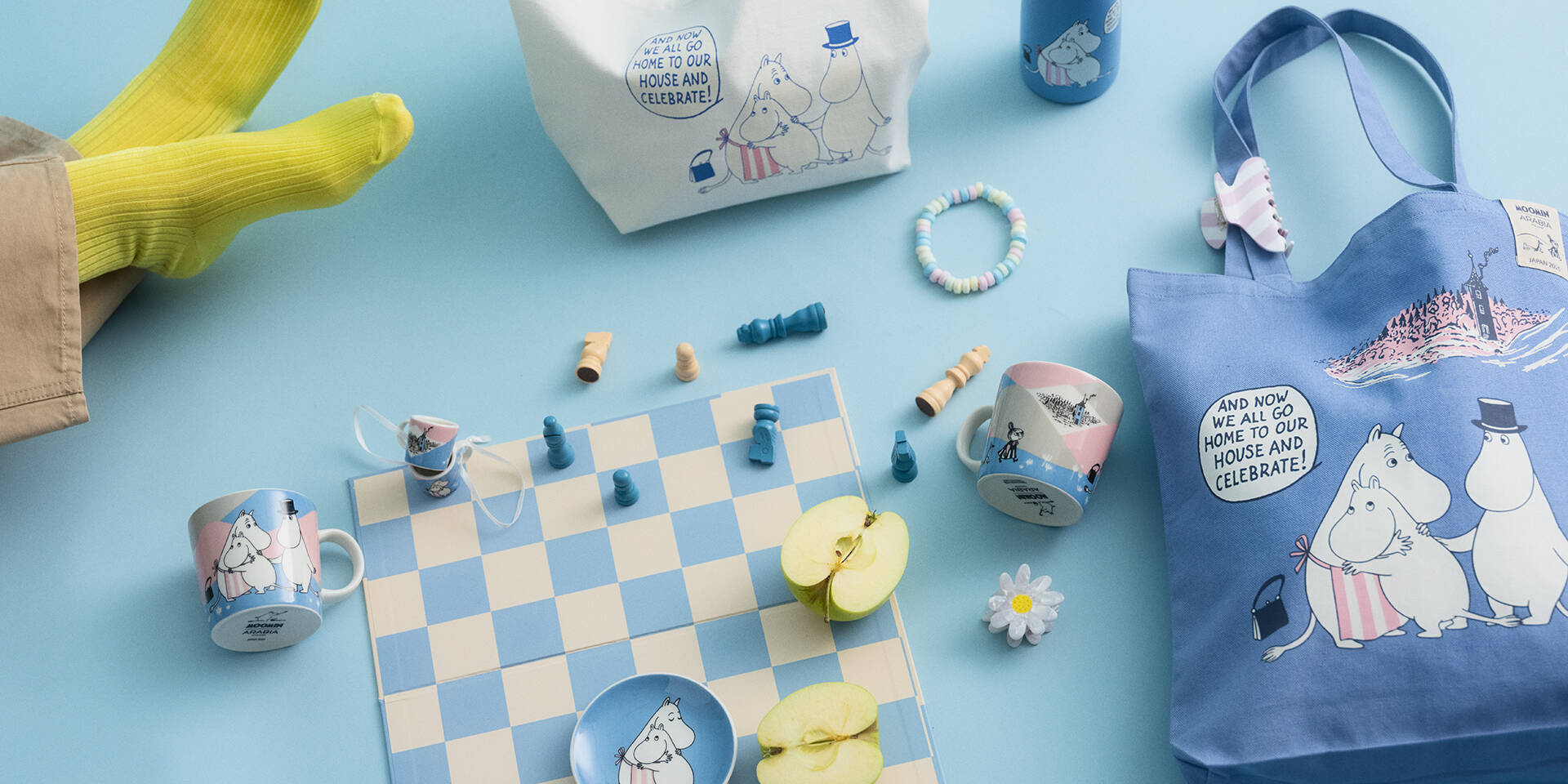 Moomin Home at last-themed products including a bag and mugs on a blue background with a chessboard