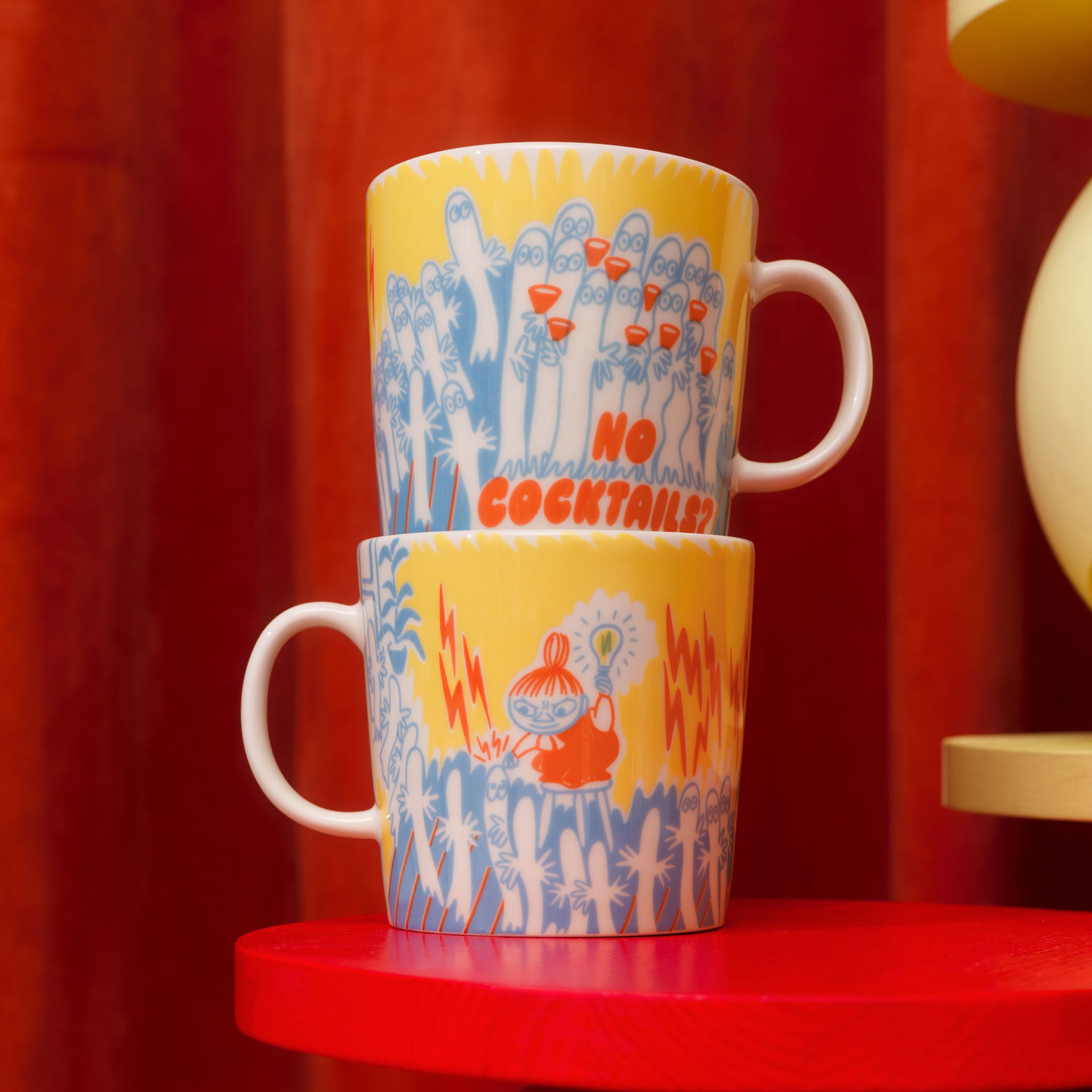 Moomin mug 0,4L Party Queue - Two Party Queue mugs stacked on a red stool with a red curtain background