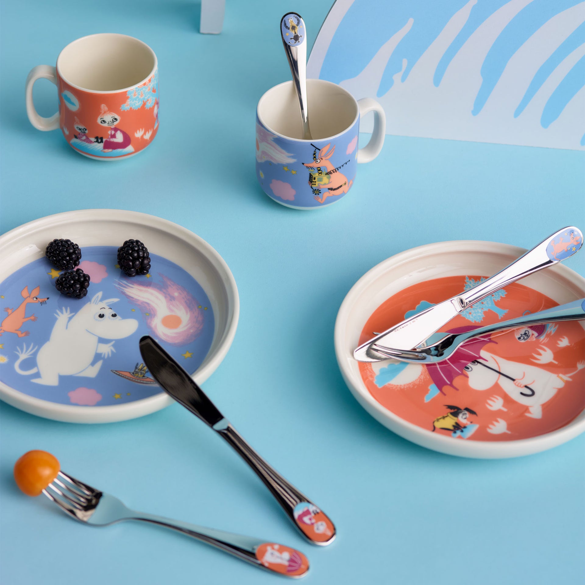 Mumin Barnset Under paraplyet - A styled flat-lay of a Space Adventure themed ceramic tableware set on a light blue background, including plates, mugs, cutlery, and utensils.