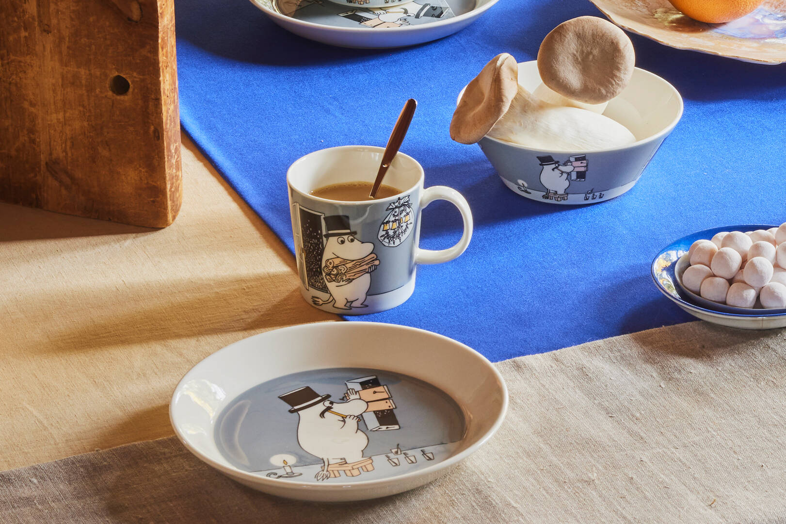 Table setting with ceramic items featuring Moominpappa  character on a blue tablecloth.
