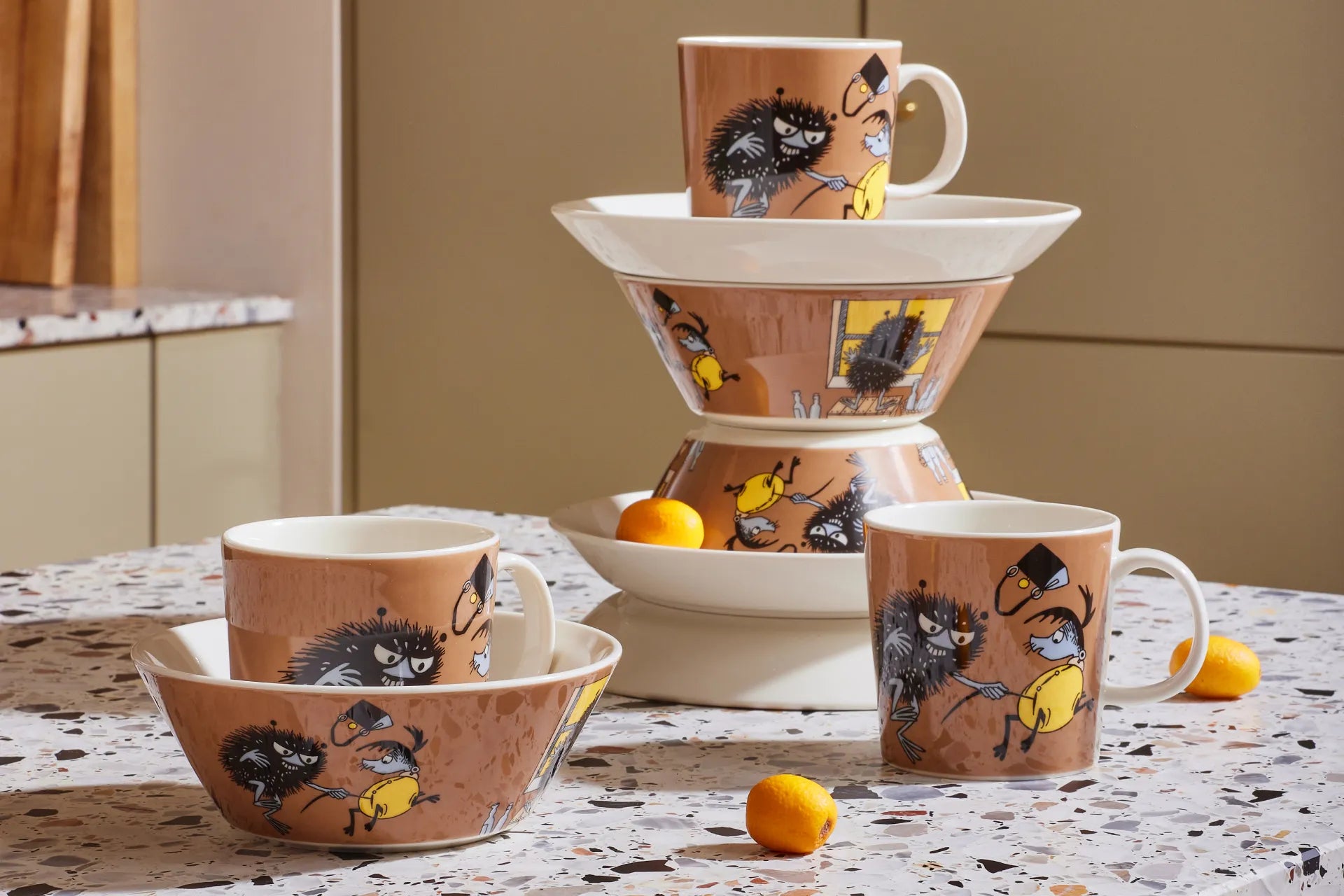 Ceramic set with cups and a bowl featuring brown Stinky illustrations on a table.