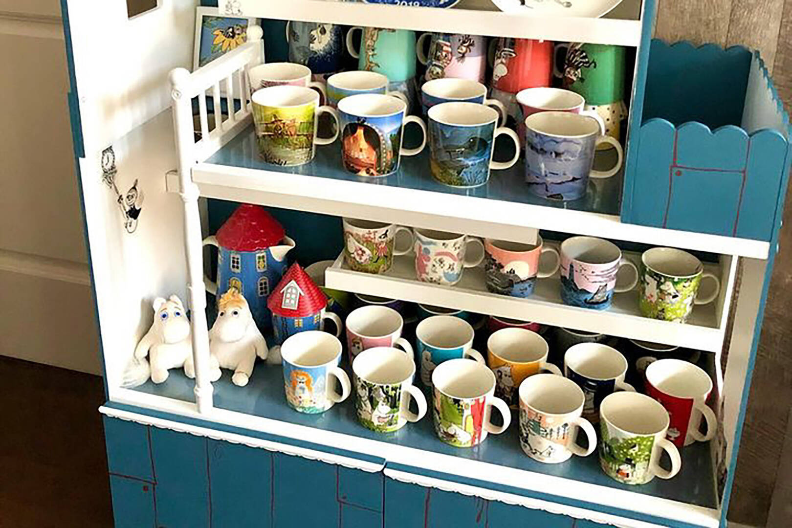 Shelf with various decorated Moomin mugs on a blue and white cabinet