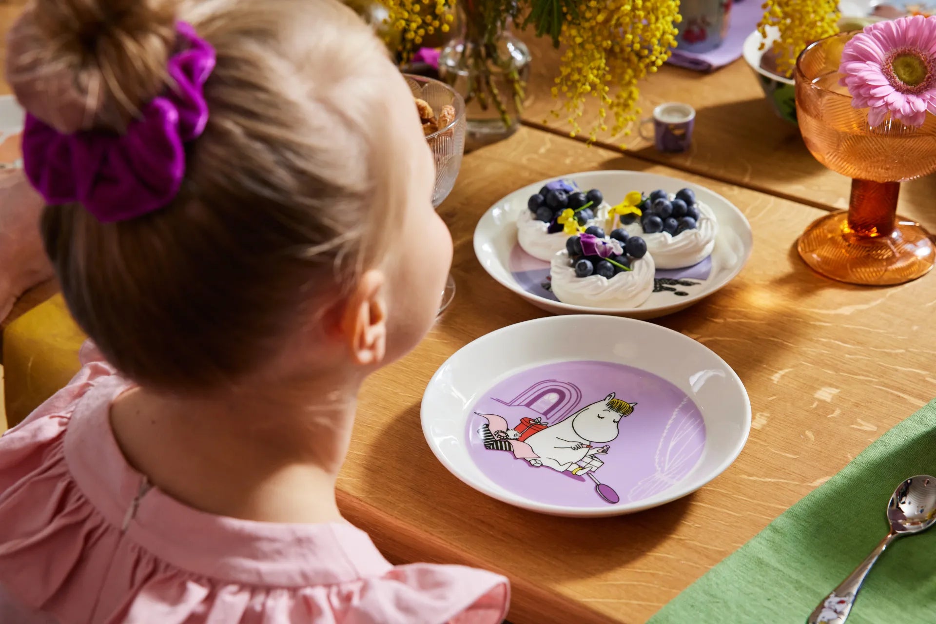 Child looking at a table with purple Snorkmaiden-decorated plate and flowers