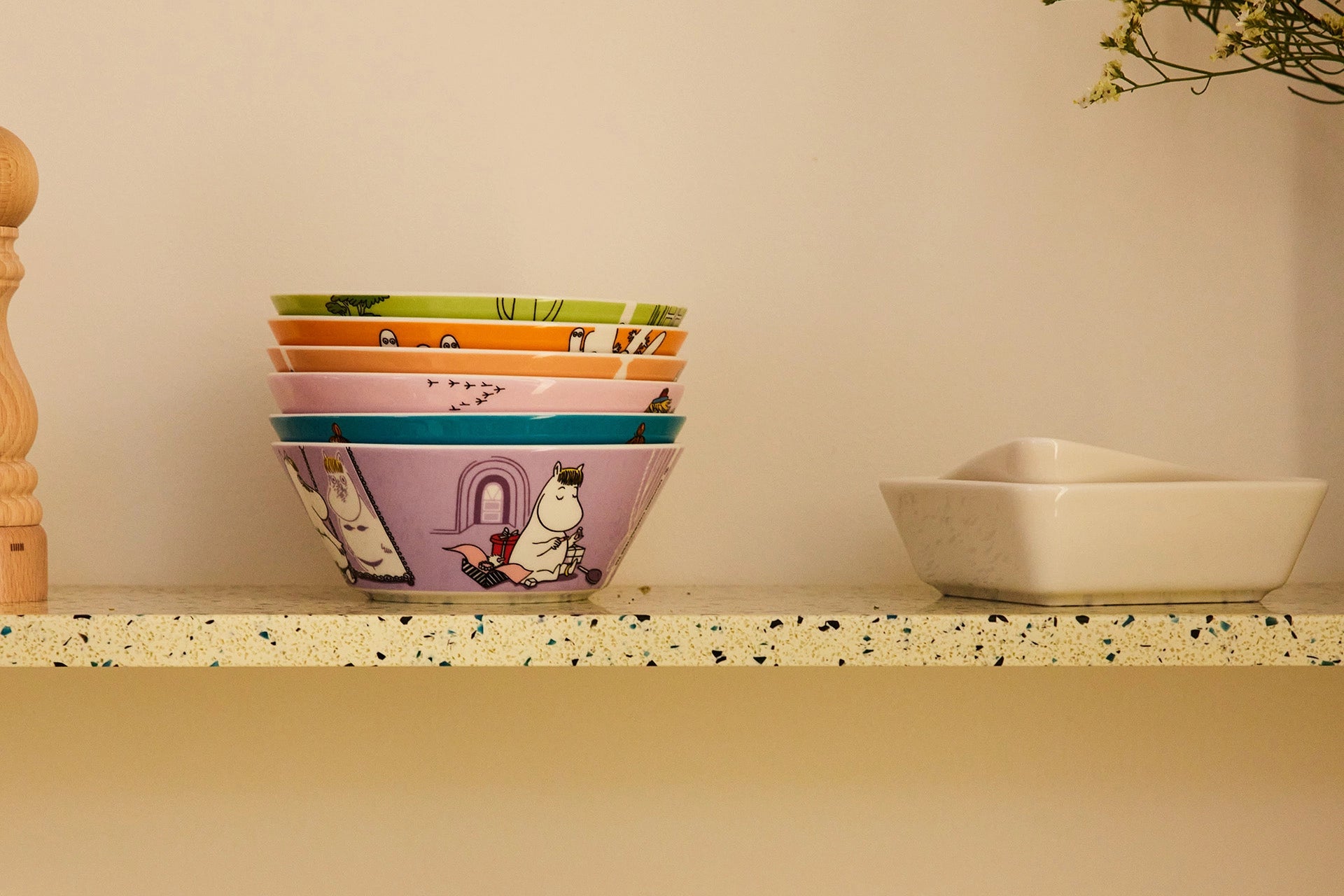 Stack of colorful Moomin Arabia Moomin characters bowls on a shelf with a plain background