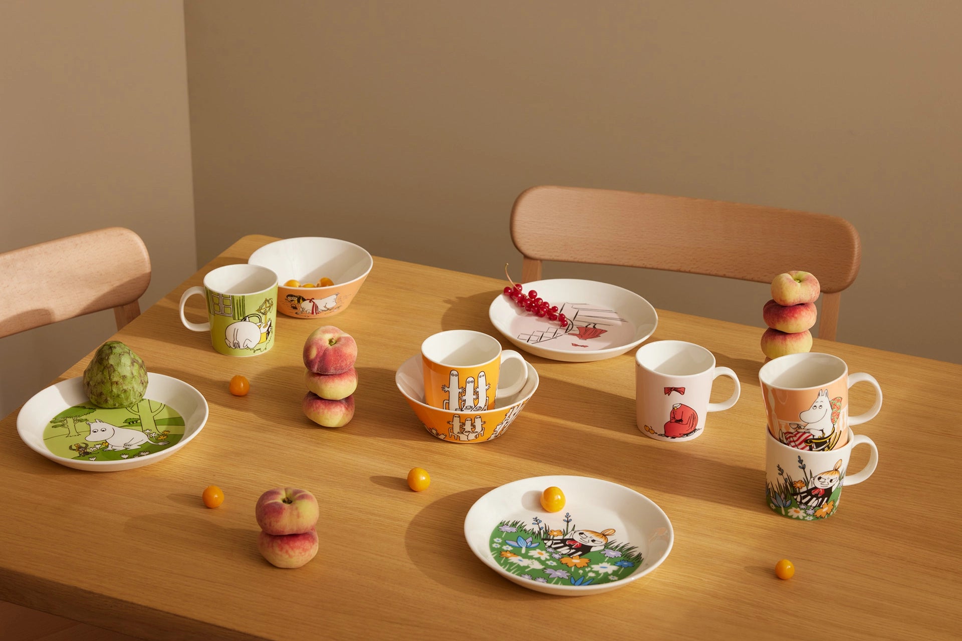 Dishes and mugs with Moomin character designs on a wooden table against a beige wall.