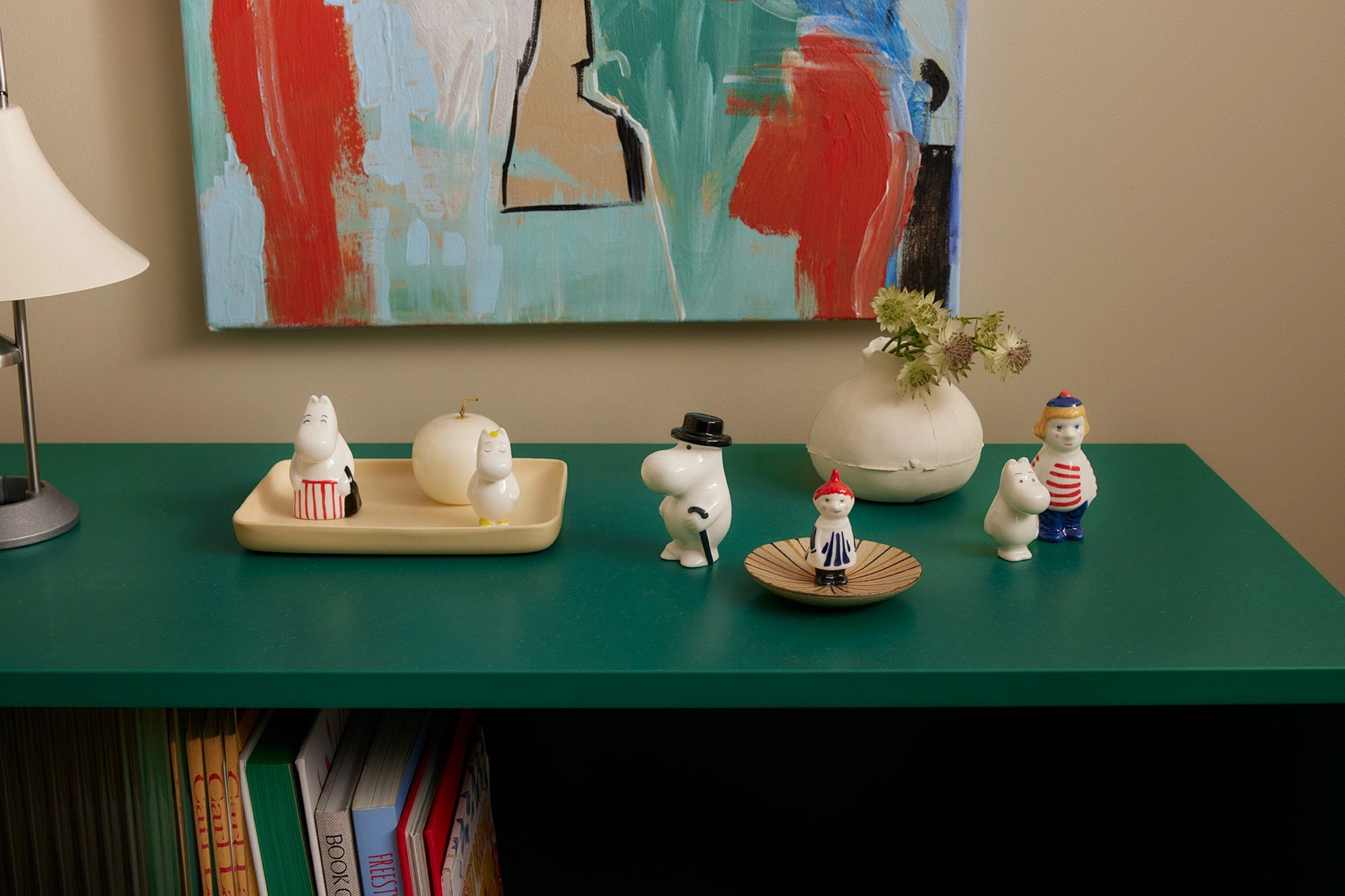 Decorative Moomin figurines on a green table with a colorful abstract painting in the background.