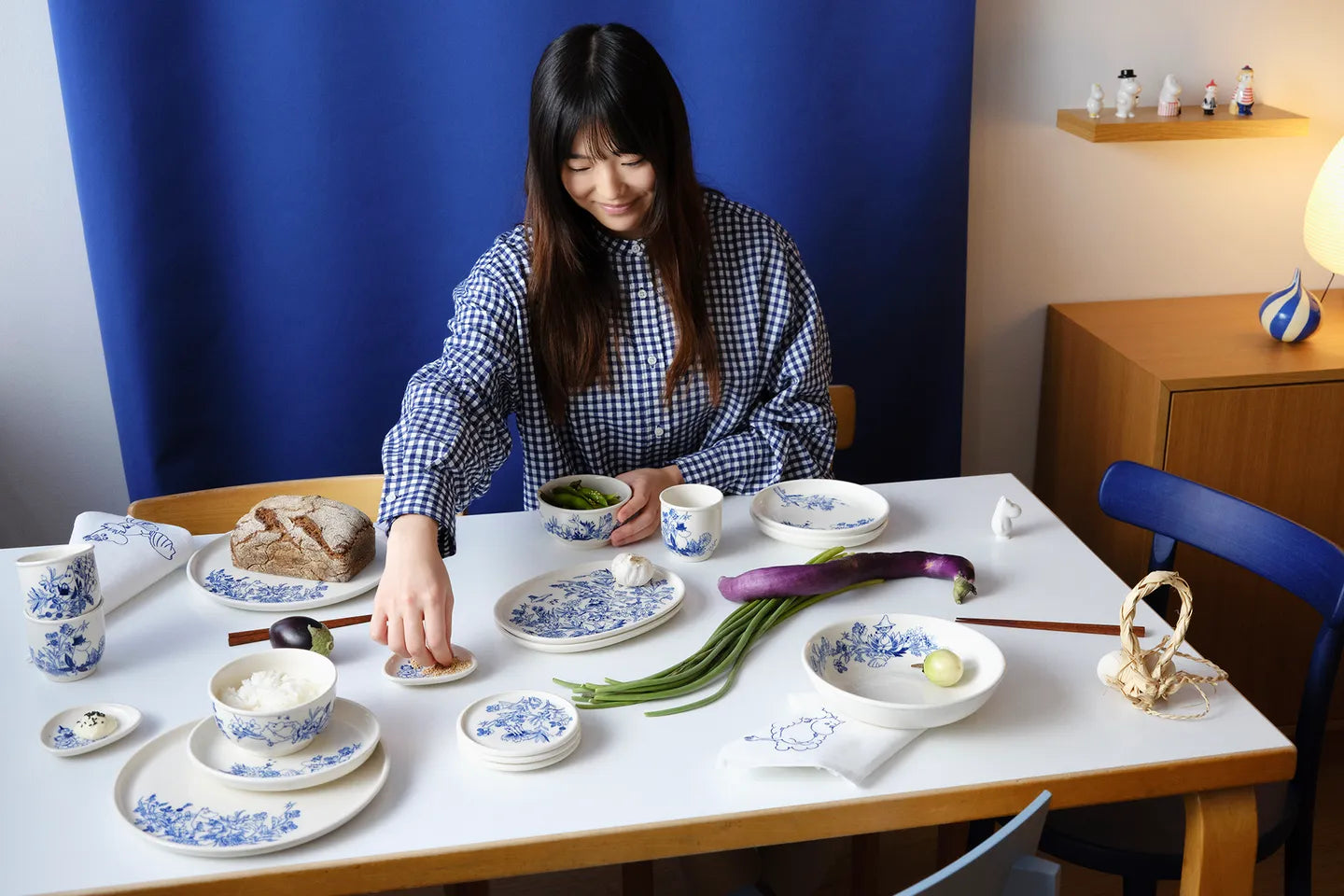 Woman arranging food on a table with various haru dishes and utensils.